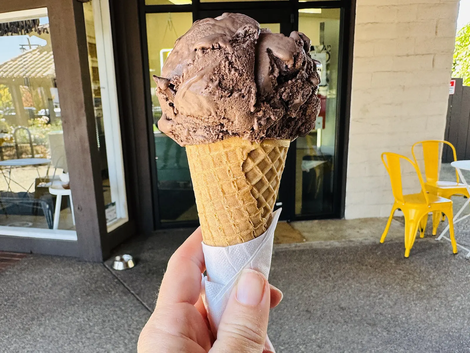 A scoop of dark chocolate chip ice cream on a waffle cone outside an ice cream shop. The photo was not taken in Brentwood.