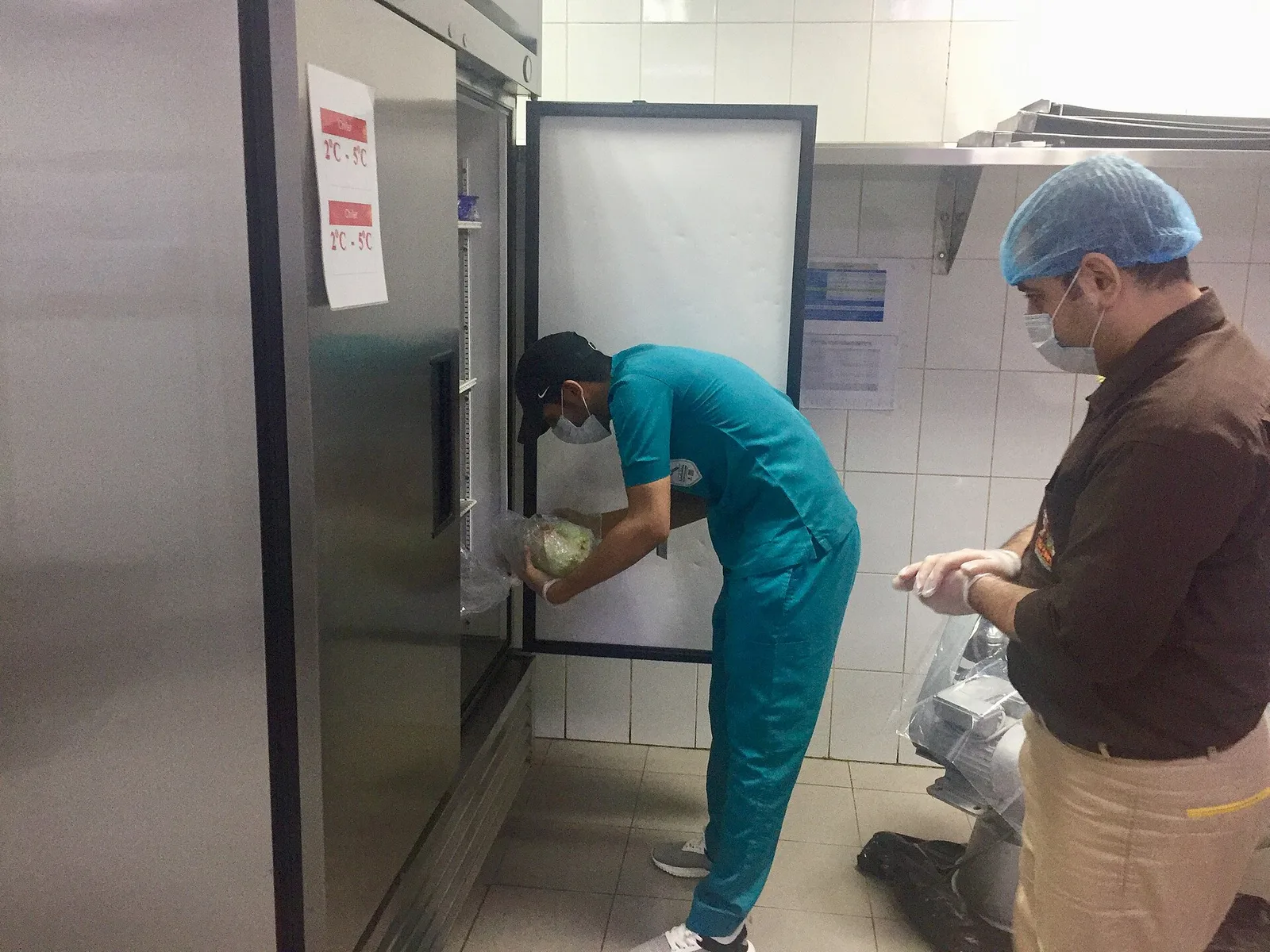 A health inspector looks over food storage in a restaurant kitchen's refrigerator